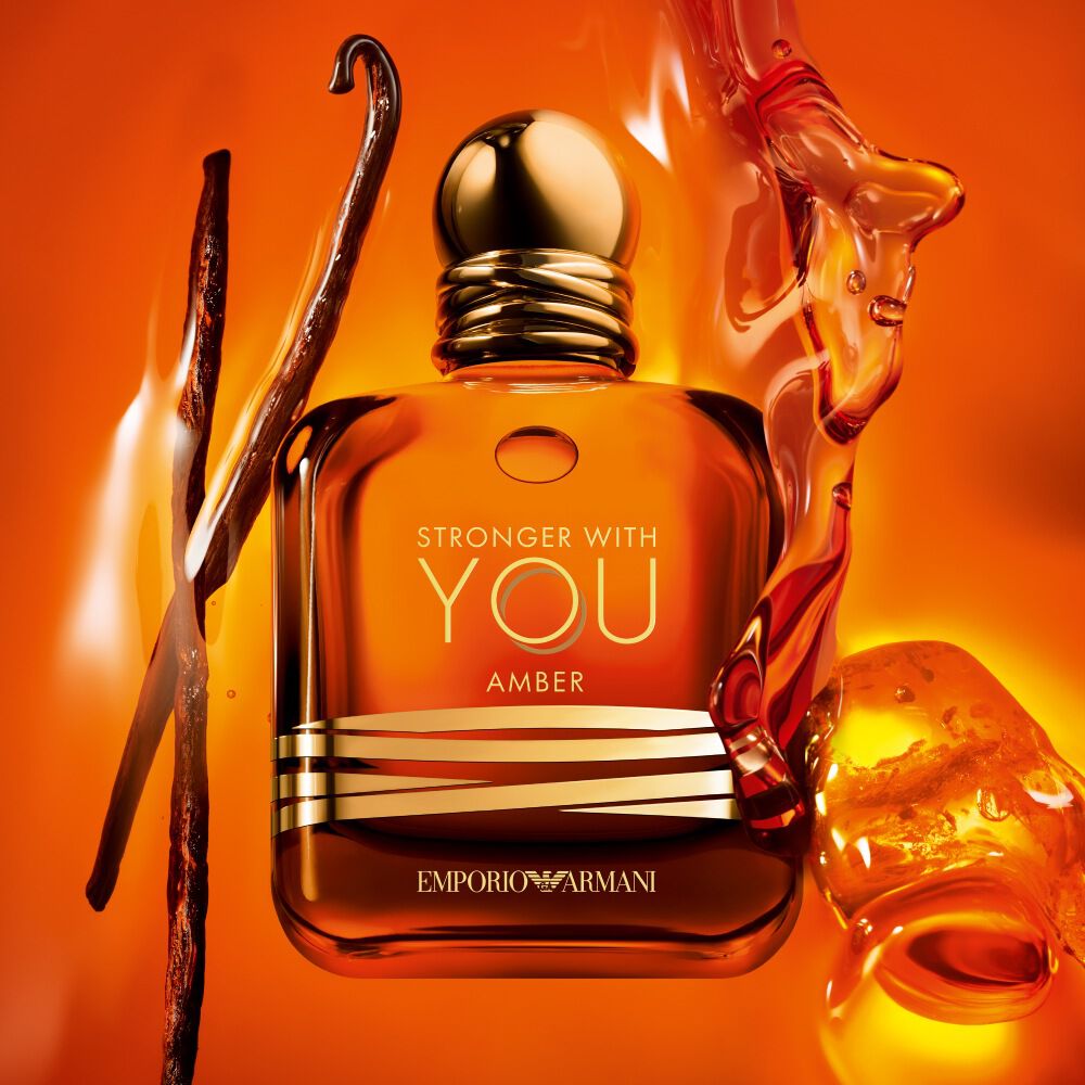 The Emporio Armani Stronger With You Amber fragrance bottle is centrally featured, accompanied by vanilla pods and amber resin, all against a vibrant amber background.
