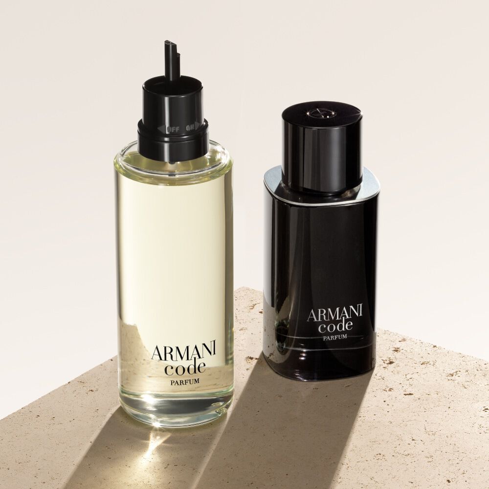 Due flaconi di Armani Code Parfum sono esposti su uno sfondo beige testurizzato. Il flacone a sinistra e una ricarica, che mostra il suo aspetto piu leggero e trasparente, mentre quello a destra mostra il classico flacone nero opaco della fragranza.