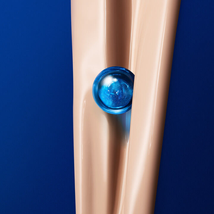 A close-up of a smooth, beige surface resembling a leg, with a blue, spherical object nestled between the knees against a vibrant blue background.