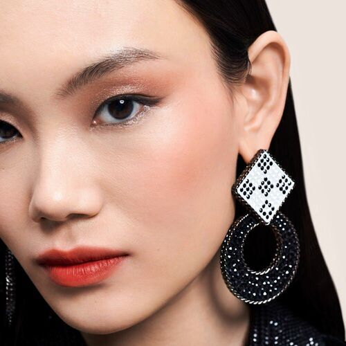 Un primo piano di una donna con lunghi capelli neri, che indossa grandi orecchini decorativi e un trucco elegante.