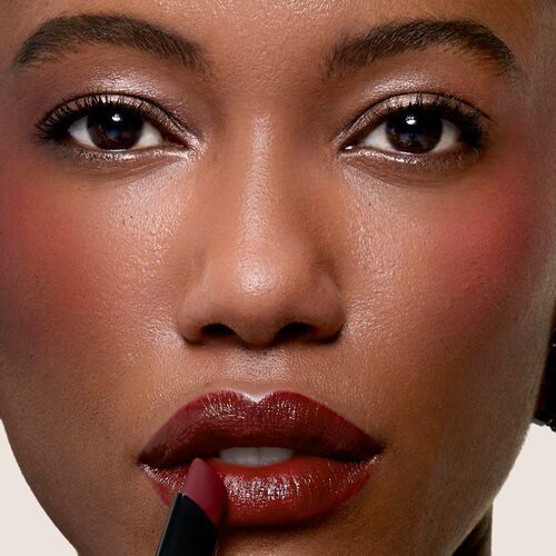 Close-up of a woman's face applying dark lipstick, showcasing her glowing skin and expressive eyes.