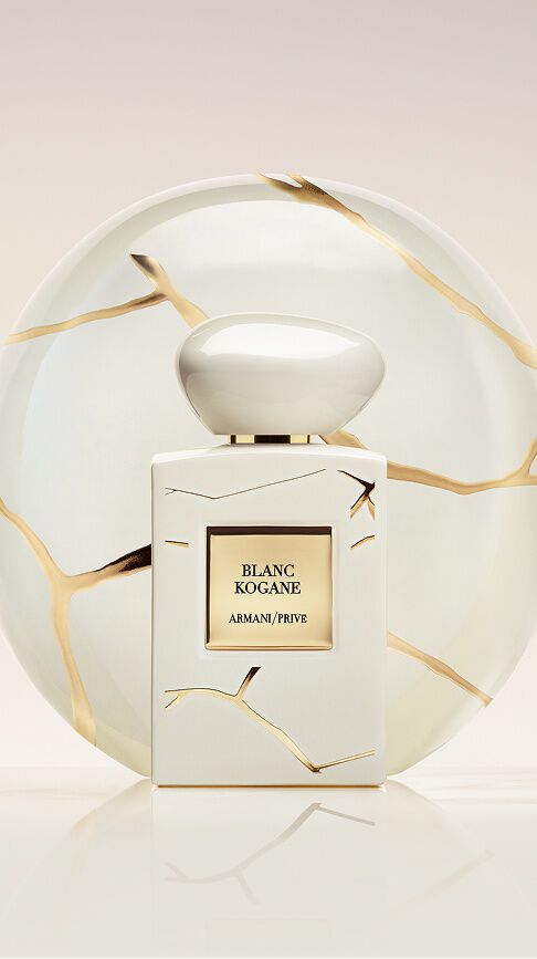 Armani/Prive Blanc Kogane: un flacone bianco puro con venature d'oro, davanti a un piatto di porcellana Kintsugi, simbolo di una femminilita serena e della radiosita solare del gelsomino e del giglio.