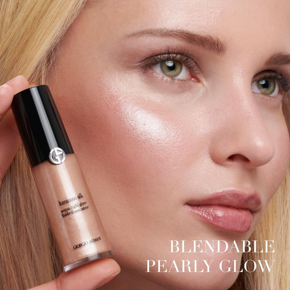 A close-up of a model's face showcasing a radiant glow, holding a bottle of Giorgio Armani illuminator with the text "Blendable Pearly Glow" nearby.