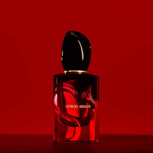 A bottle of Giorgio Armani perfume with a sleek design, set against a rich red background.