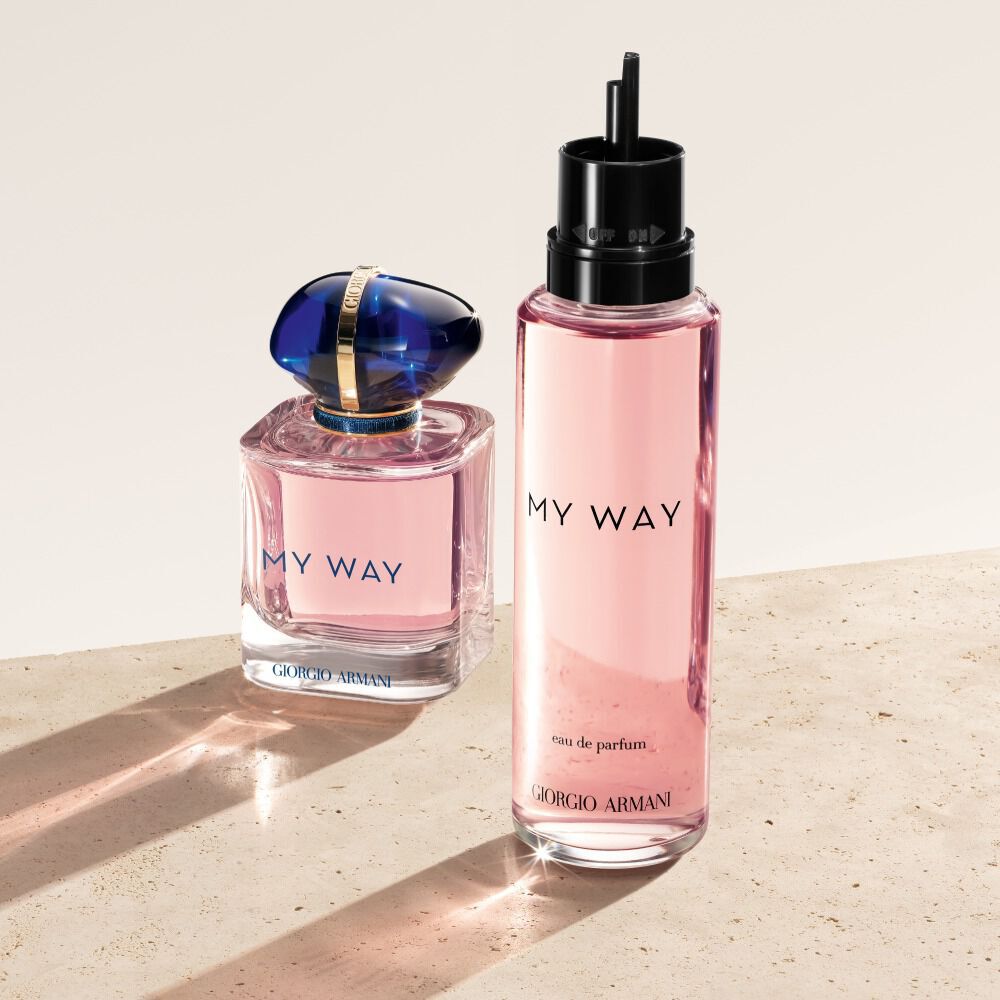 Una bottiglia e una ricarica di Giorgio Armani My Way Eau de Parfum. La bottiglia originale, di un rosa tenue con un tappo blu, e posizionata accanto alla sua controparte ricaricabile, piu alta e di un rosa traslucido. Poggiano su una superficie chiara e testurizzata.