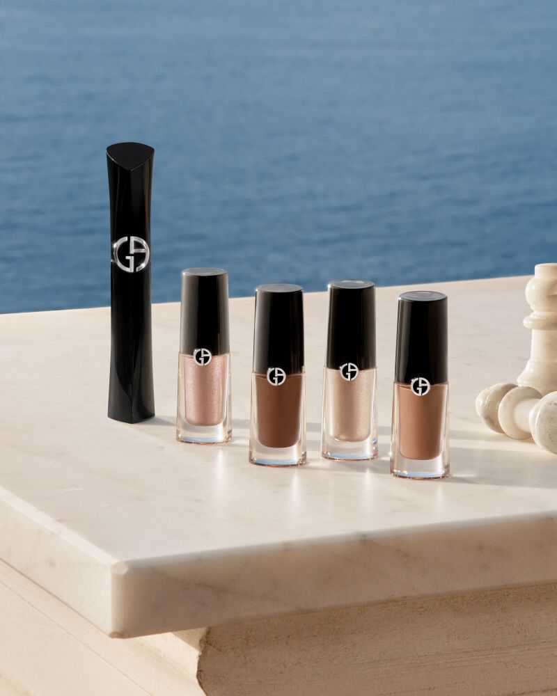 Essenziali occhi Armani: mascara e Eye Tint con pezzi di scacchi su marmo davanti al mare. Simbolo di bellezza strategica ed eleganza costiera spontanea per una radiosita estiva assoluta firmata dalla Maison.