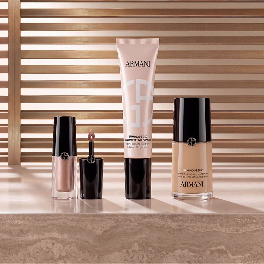  Prodotti di make-up Armani beauty tra cui illuminante liquido, il primer illuminante Luminous Silk e il fondotinta Luminous Silk esposti su una superficie in marmo con uno sfondo caldo a listelli.