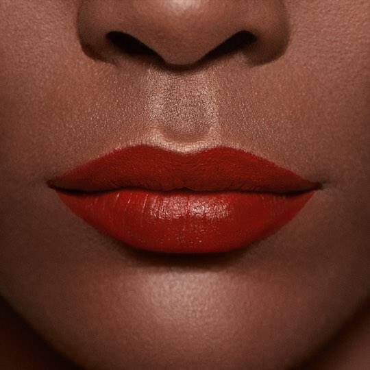 Close-up of a pair of full lips painted with bright red lipstick, against a smooth, dark skin tone.