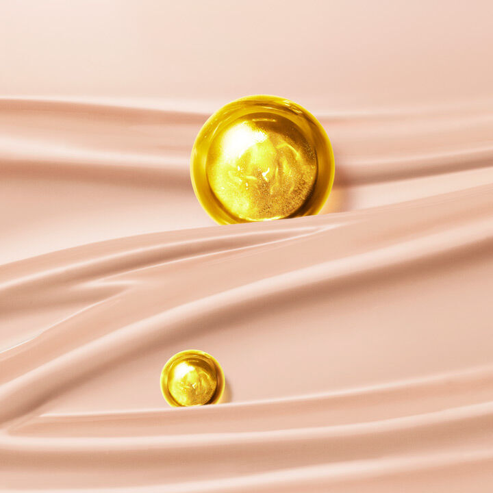A golden sphere and a smaller golden sphere resting on softly draped, light pink fabric.