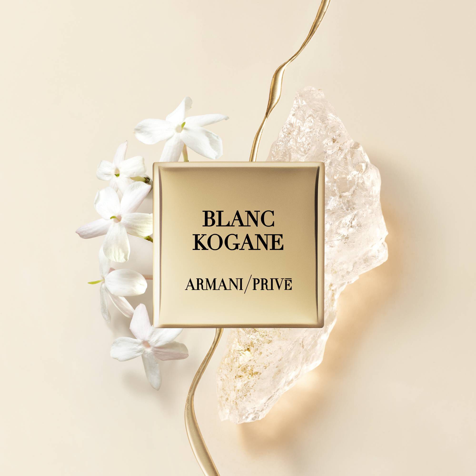 A stylish perfume bottle labeled "BLANC KOGANE" by Armani Prive, surrounded by white flowers and a crystal fragment on a soft beige background.