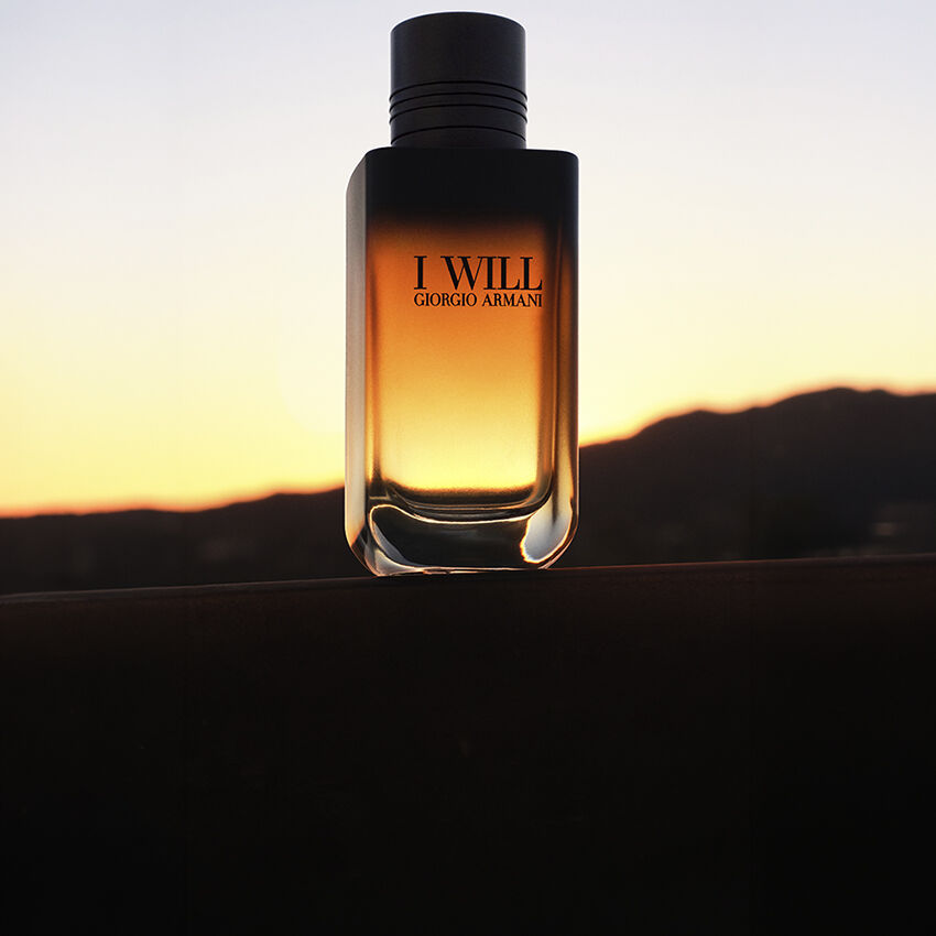 Flacone della fragranza I WILL di Giorgio Armani su uno sfondo di paesaggio al tramonto.