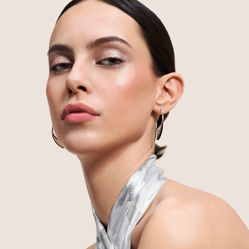 Ritratto di una giovane donna con trucco elegante, orecchini d'argento e un foulard lucido, su sfondo neutro.