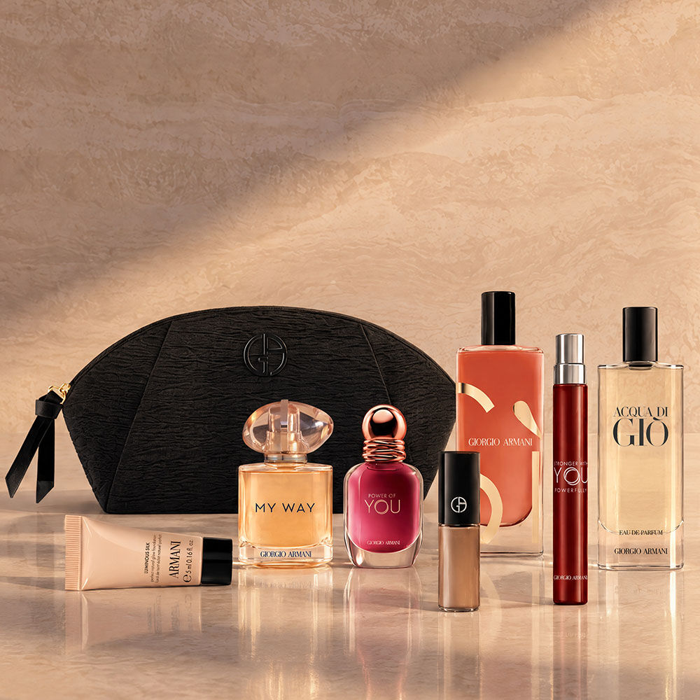 Una pochette nera Armani Beauty con fragranze, make-up e prodotti skincare su uno sfondo beige.
