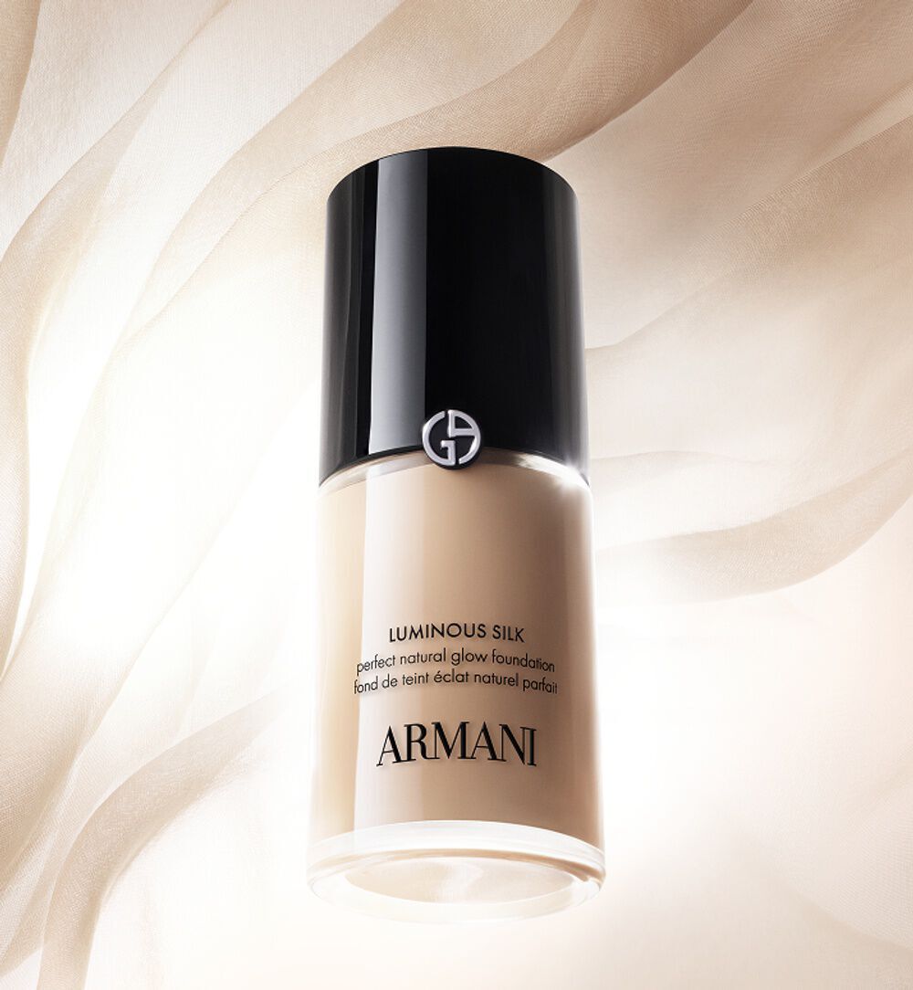 Image Armani Luminous Silk foundation bottle in beige packaging surrounded by dewdrops on a golden beige background.
