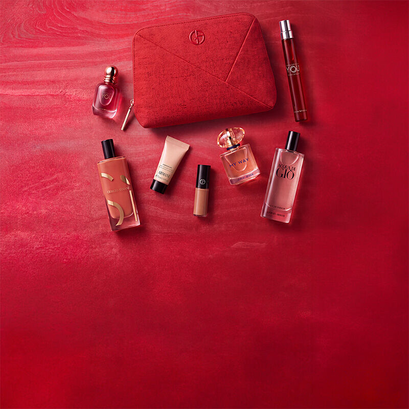 Tre prodotti Armani Beauty — un prodotto labbra, la fragranza Power of You e il fondotinta Luminous Silk — su uno sfondo rosso materico.