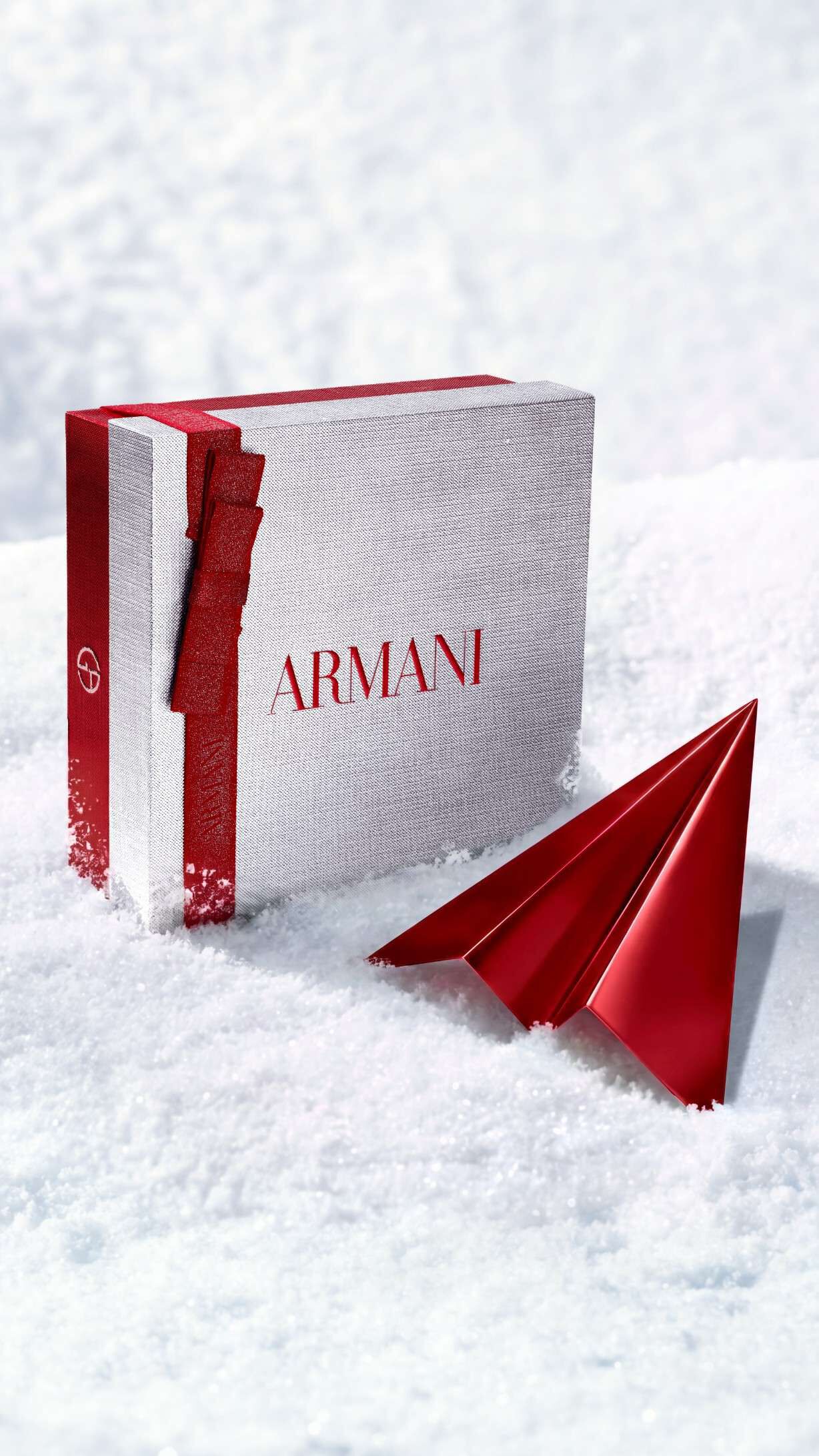 Confezione regalo argentata Armani Beauty con un aeroplanino di carta rosso che rappresenta la consegna gratuita per le feste.