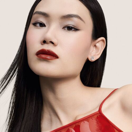 Ritratto di una giovane donna con trucco elegante, indossa orecchini brillanti e un top rosso traslucido.