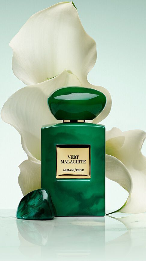 Armani/Prive Vert Malachite: un vibrante flacone verde smeraldo con tappo in pietra, davanti a candidi gigli bianchi, che cattura la radiosa freschezza di un giardino russo avvolto in una bellezza luminosa e serena.