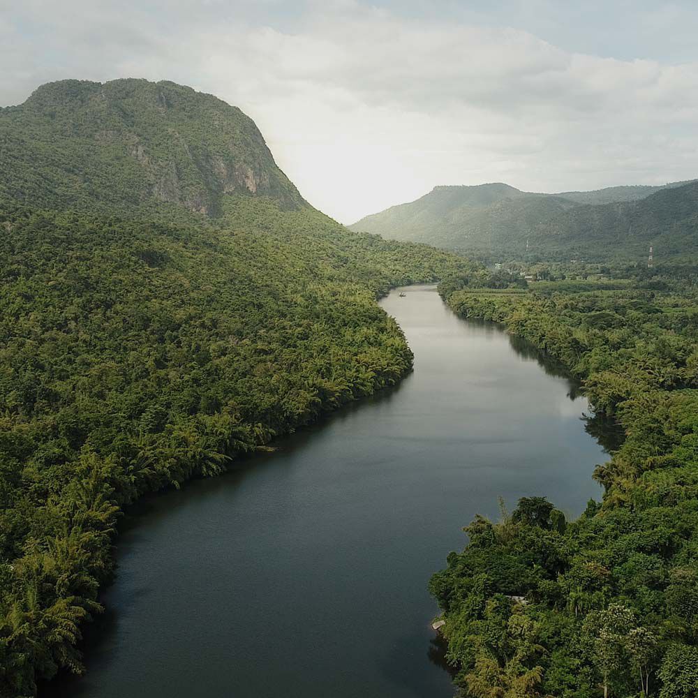 A serene landscape featuring a winding river surrounded by lush green forests and mountains under a cloudy sky.
