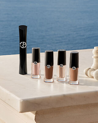 Essenziali occhi Armani: mascara e Eye Tint con pezzi di scacchi su marmo davanti al mare. Simbolo di bellezza strategica ed eleganza costiera spontanea per una radiosita estiva assoluta firmata dalla Maison.