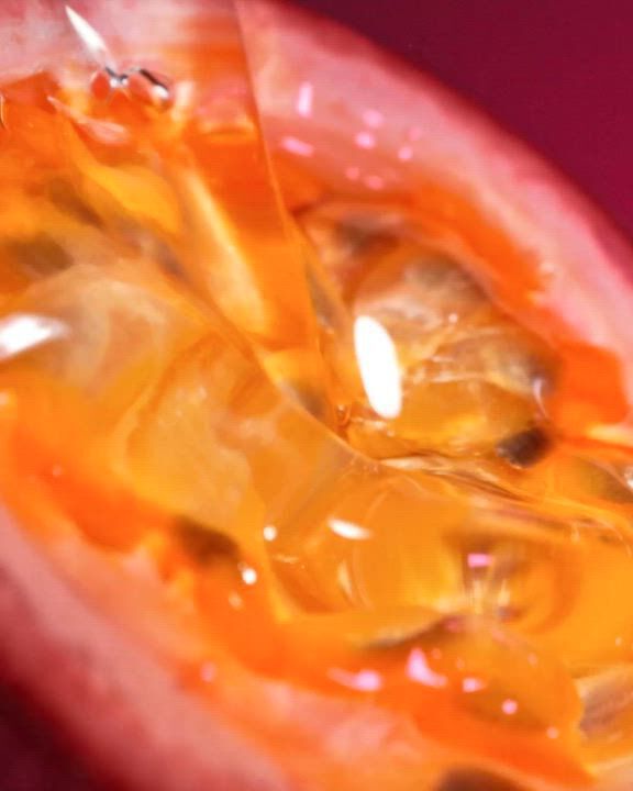  Un primissimo piano di una maracuja (frutto della passione) tagliata, che mostra i semi succosi di un arancione vivace e la polpa in ogni dettaglio. L'immagine ha una consistenza calda e lucida. Sovrapposto in testo bianco c'e la descrizione: "Un'esplosione aspra e succosa di Maracuja (Frutto della Passione) con il delizioso calore sensuale della Vaniglia". In basso, sono presenti un link "SCOPRI" e un'icona play bianca.