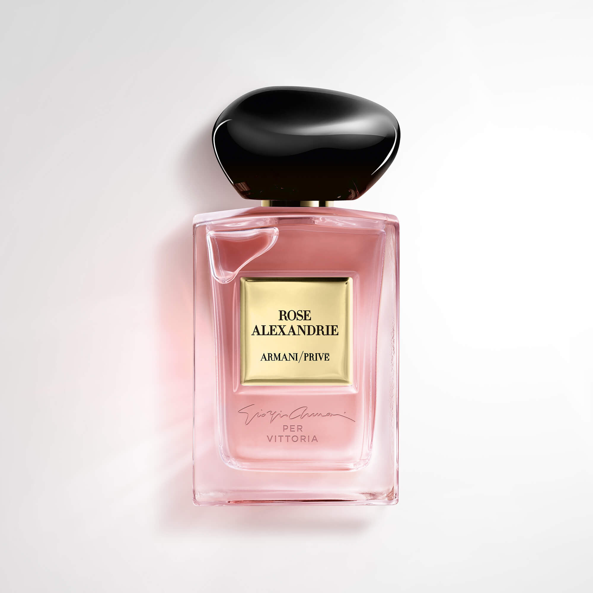 A glass perfume bottle with a pink liquid, featuring a black cap and a golden label that reads "ROSE ALEXANDRIE" and "ARMANI/PRIVE." The bottle has a sleek, elegant design.