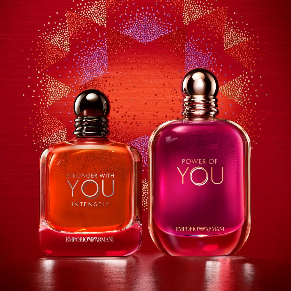 Due fragranze Emporio Armani, Stronger With You Intensely e Power of You, su uno sfondo rosso festivo.​