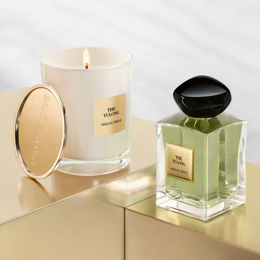 A luxury scented candle and a perfume bottle displayed elegantly on a golden surface, both featuring branding from Armani Prive.