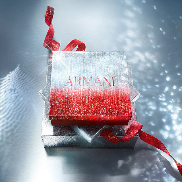 Confezione regalo Armani luccicante con nastro rosso su superficie brillante.