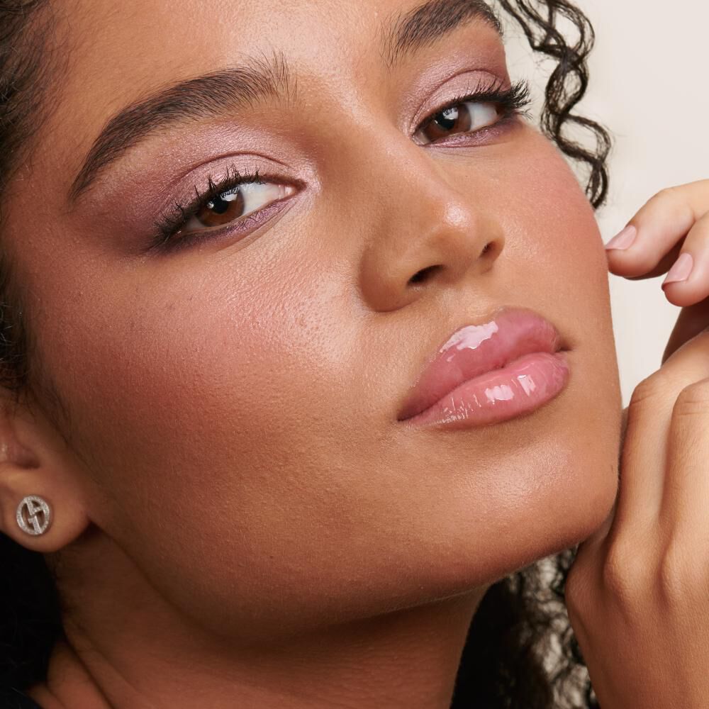 A close-up portrait of a person with curly hair, wearing soft makeup that highlights their eyes and lips, with a natural skin glow.