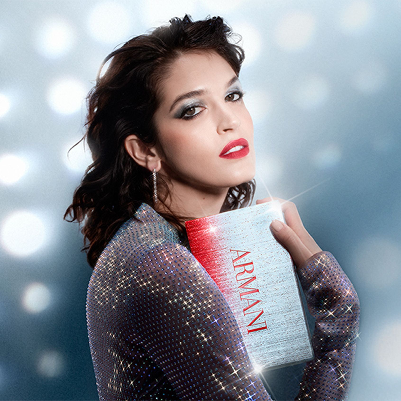 Una bellissima donna con un trucco a tema natalizio tiene una scatola regalo festiva, su uno sfondo di punti luce sognanti in stile disco.