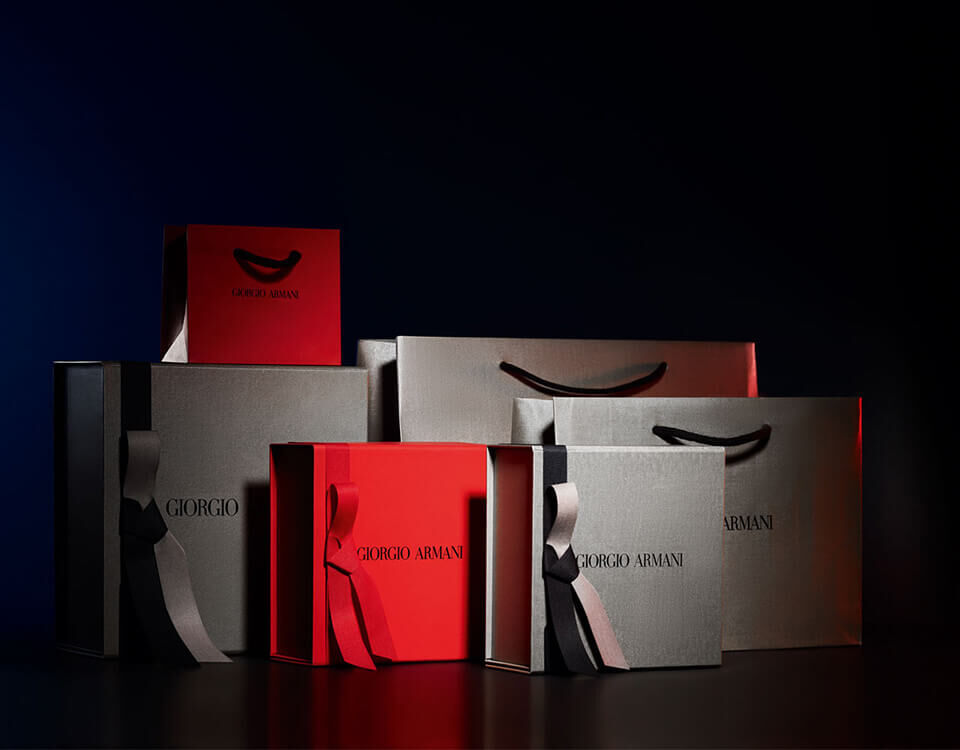 A collection of stylish gift boxes in various sizes, featuring the Giorgio Armani logo, with a mix of red and black colors, set against a dark background.