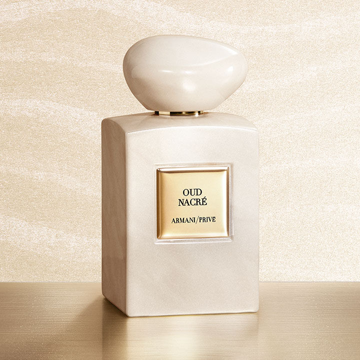 Armani/Prive Oud Nacre: un flacone perlato e iridescente con tappo scolpito, su un piedistallo dorato davanti a uno sfondo scintillante. Un luminoso omaggio alla nobilta dell'Oud e all'arte della profumeria d'eccellenza firmata Armani Beauty.