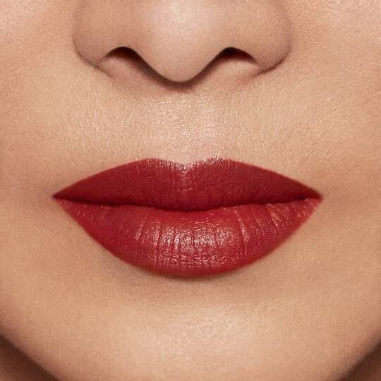 Close-up of a pair of lips coated in a rich red lipstick, with a smooth and defined shape. The skin around the lips is textured and even-toned.