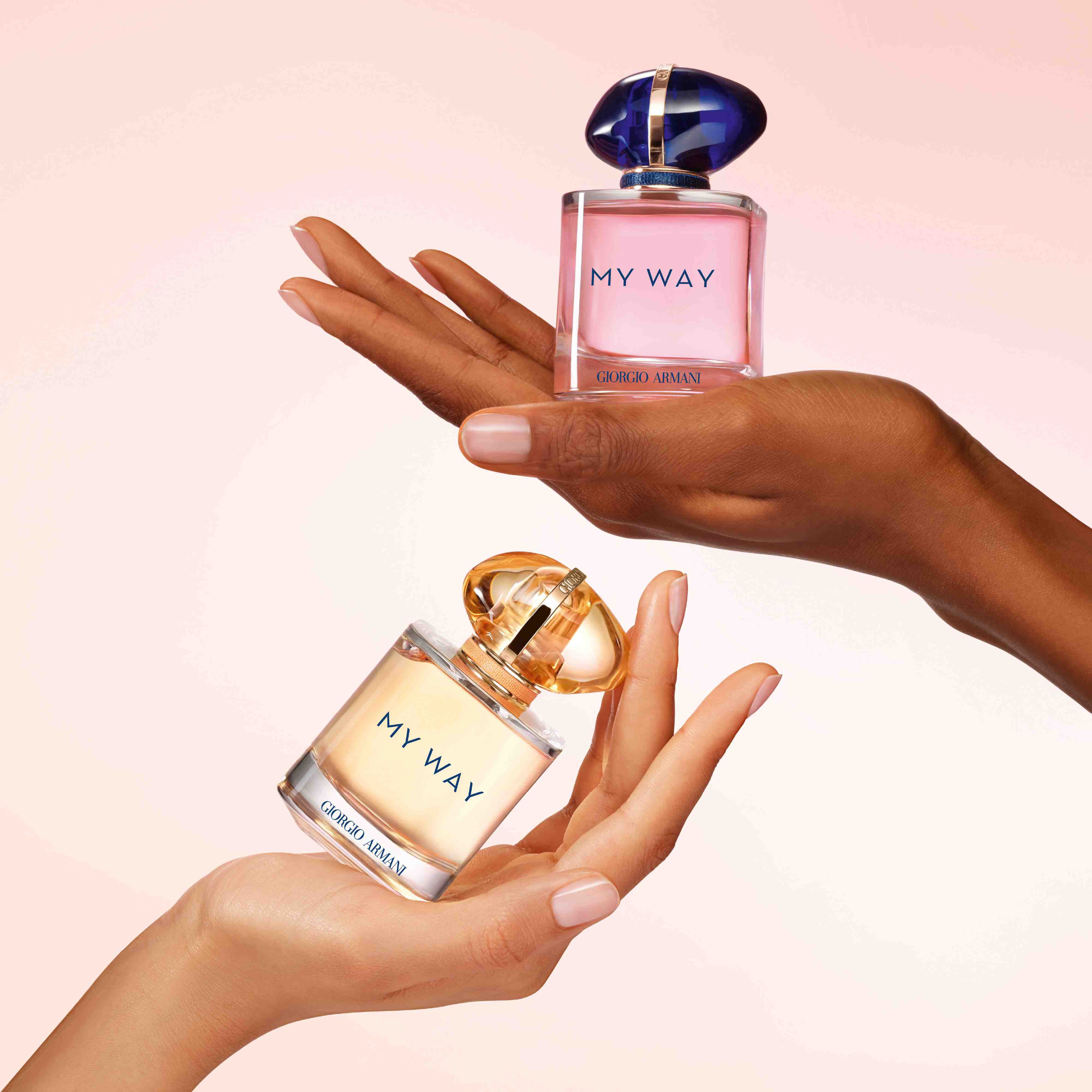 Due mani con diverse tonalita di pelle che reggono ciascuna un flacone del profumo My Way di Giorgio Armani.