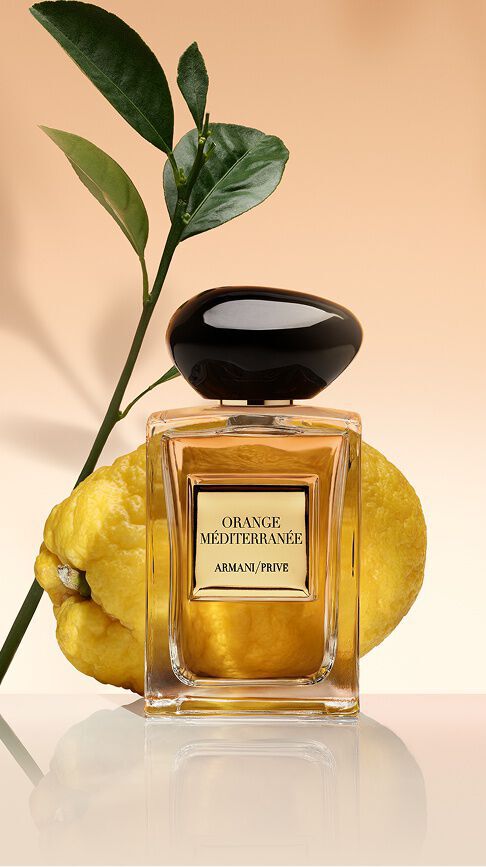 Armani/Prive Orange Mediterranee: un flacone dal nettare dorato, davanti a un agrume fresco e foglie verdi, che irradia il calore solare del Mediterraneo.
