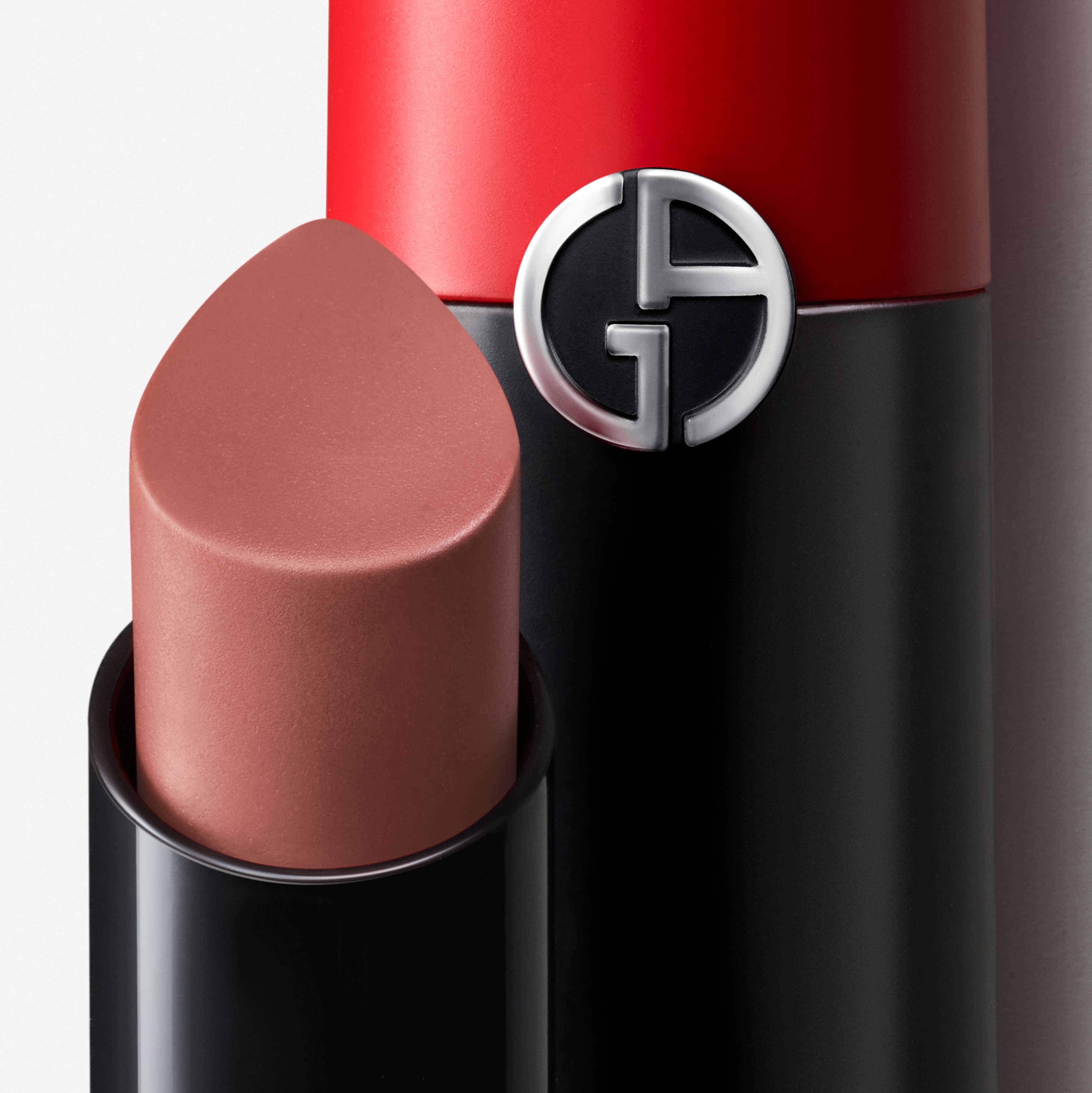 Close-up of a bullet lipstick in a sleek black and red tube, featuring a silver logo with the letters "G." The lipstick itself is a muted, warm brown shade.