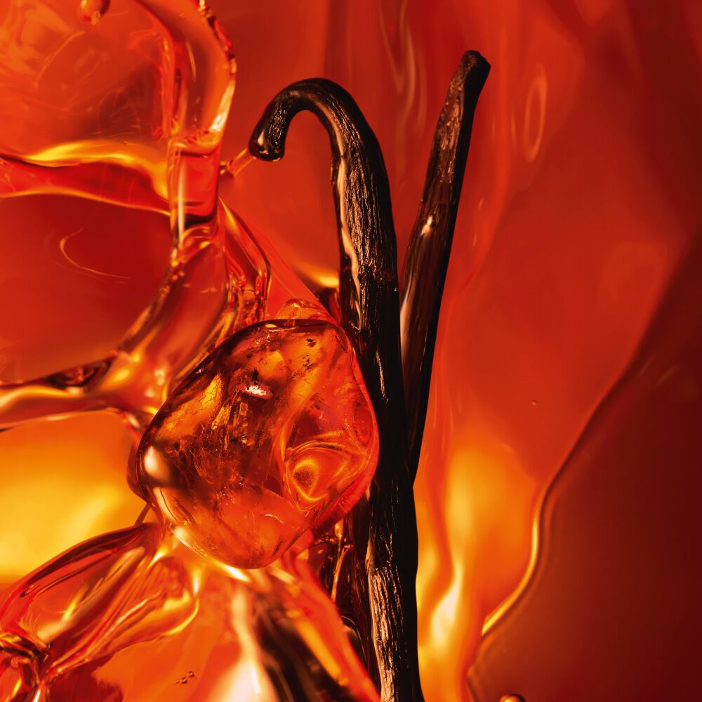 Un primo piano di due baccelli di vaniglia scuri e resina d ambra scintillante su uno sfondo ambrato caldo e luminoso.