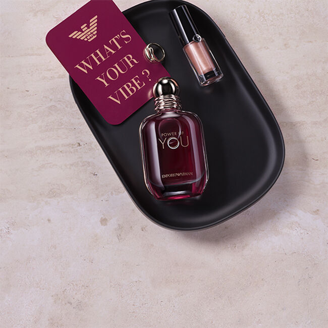 Flacone della fragranza Power of You di Emporio Armani e prodotto labbra metallizzato su un vassoio nero, accanto a una card con la scritta “What’s Your Vibe?”.