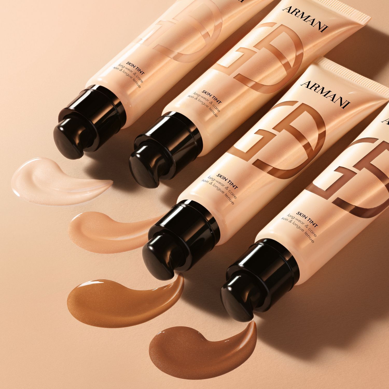 Quattro tubetti di Armani Skin Tint con campioni applicati che mostrano una gamma di tonalita.
