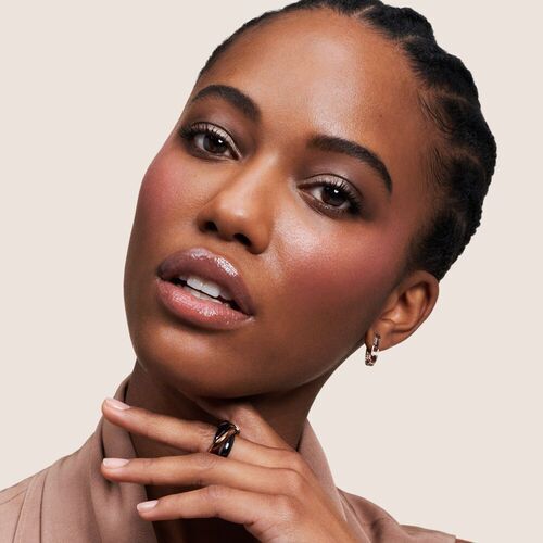 Ritratto di una donna con pelle luminosa e capelli intrecciati, indossa orecchini eleganti e un anello raffinato.