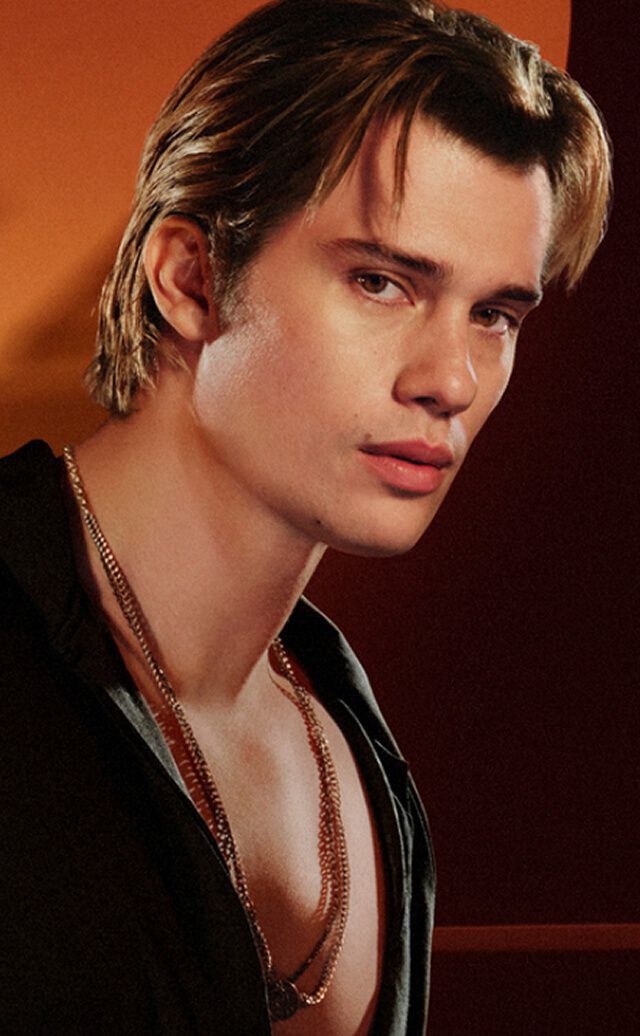  Una pubblicita per la linea di fragranze "Stronger With You" di Emporio Armani. A sinistra, un giovane uomo con capelli castano chiaro indossa una camicia nera e collane d'argento, guardando verso la fotocamera con uno sguardo serio. A destra, un carosello di prodotti sotto il titolo "EVERY FACET OF STRONGER WITH YOU" mostra tre diverse boccette di profumo. La boccetta centrale evidenziata e "Stronger With You Powerfully" nel formato da 50 ml, al prezzo di £74.00, con un pulsante "AGGIUNGI AL CARRELLO" sottostante. Sono visibili anche frecce di navigazione e una barra di scorrimento.