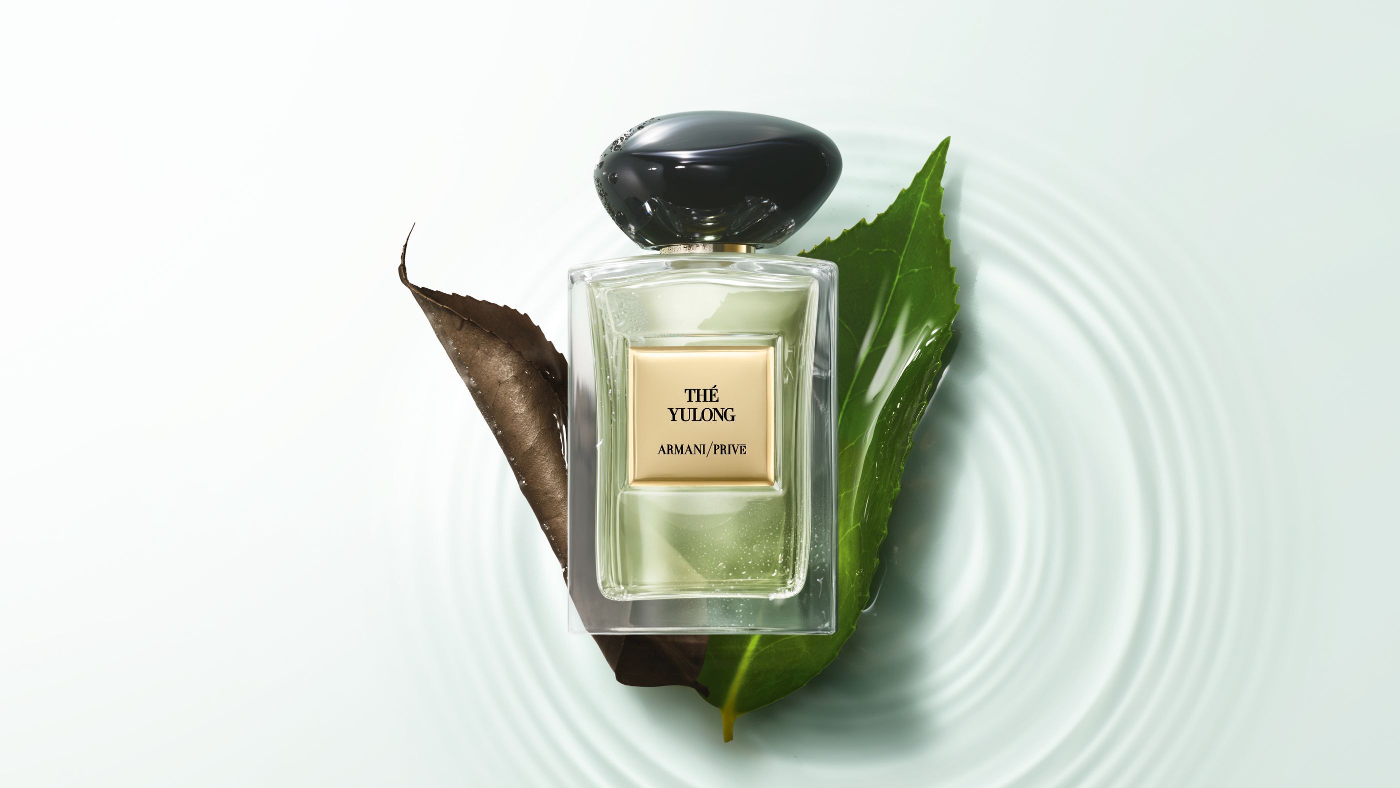 Flacone di profumo Armani/Prive "The Yulong" appoggiato su foglie sopra acqua increspata.