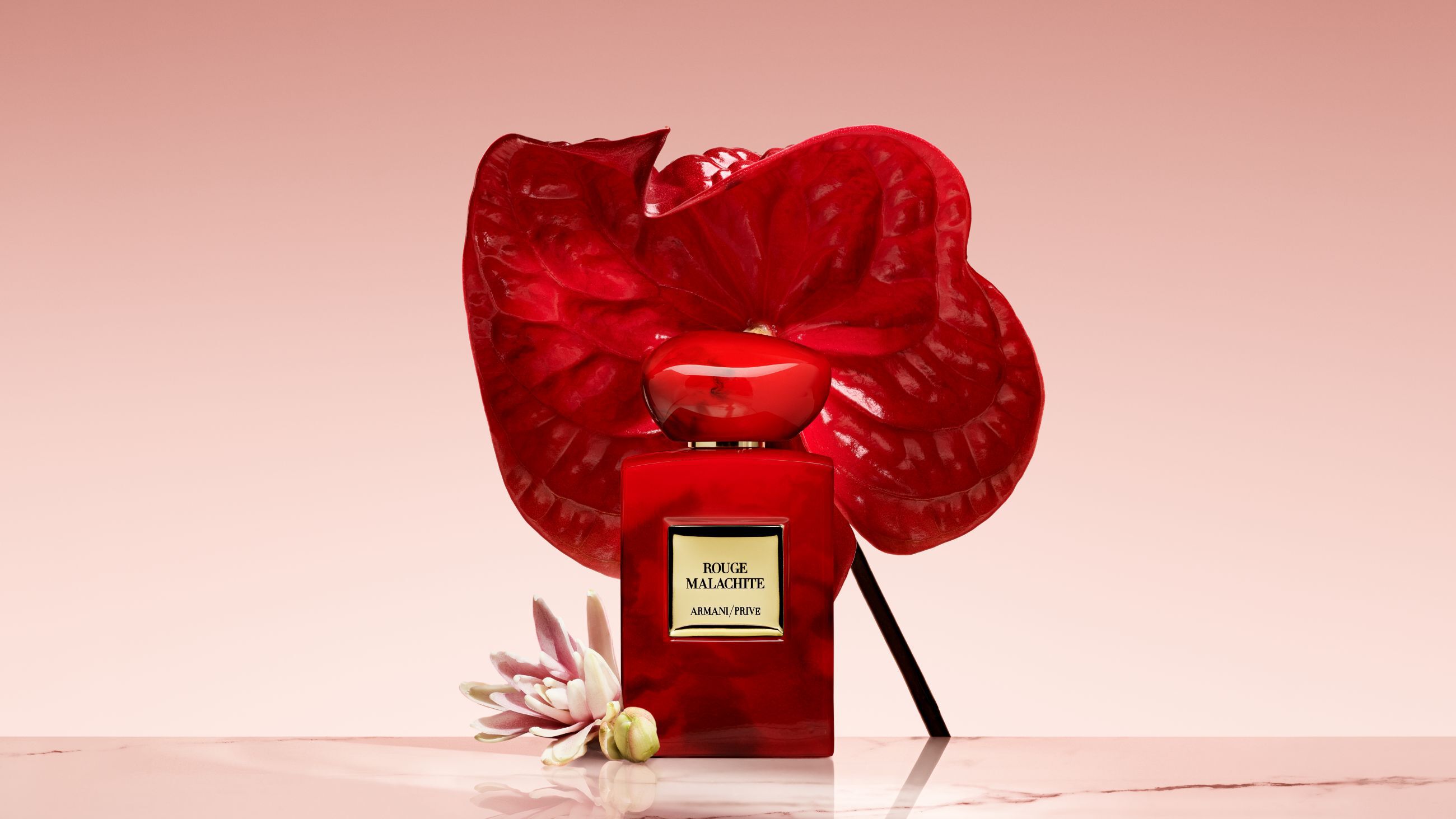 Flacone di profumo Armani/Prive Rouge Malachite davanti a un grande fiore rosso acceso.