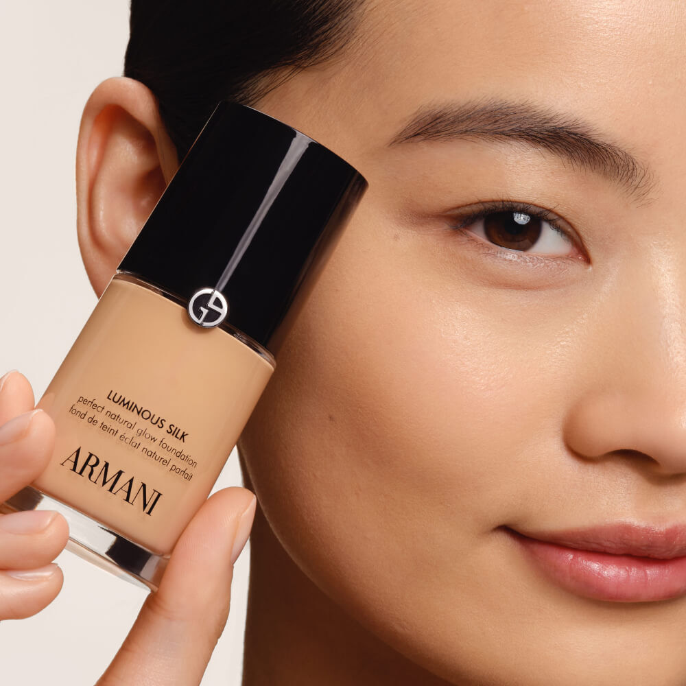A model holding a Giorgio Armani LUMINOUS SILK FOUNDATION bottle, emphasizing its natural radiance.