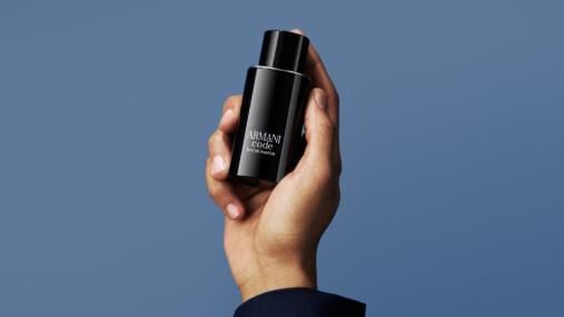 A hand holds a sleek black bottle of Armani Code cologne against a blue background.