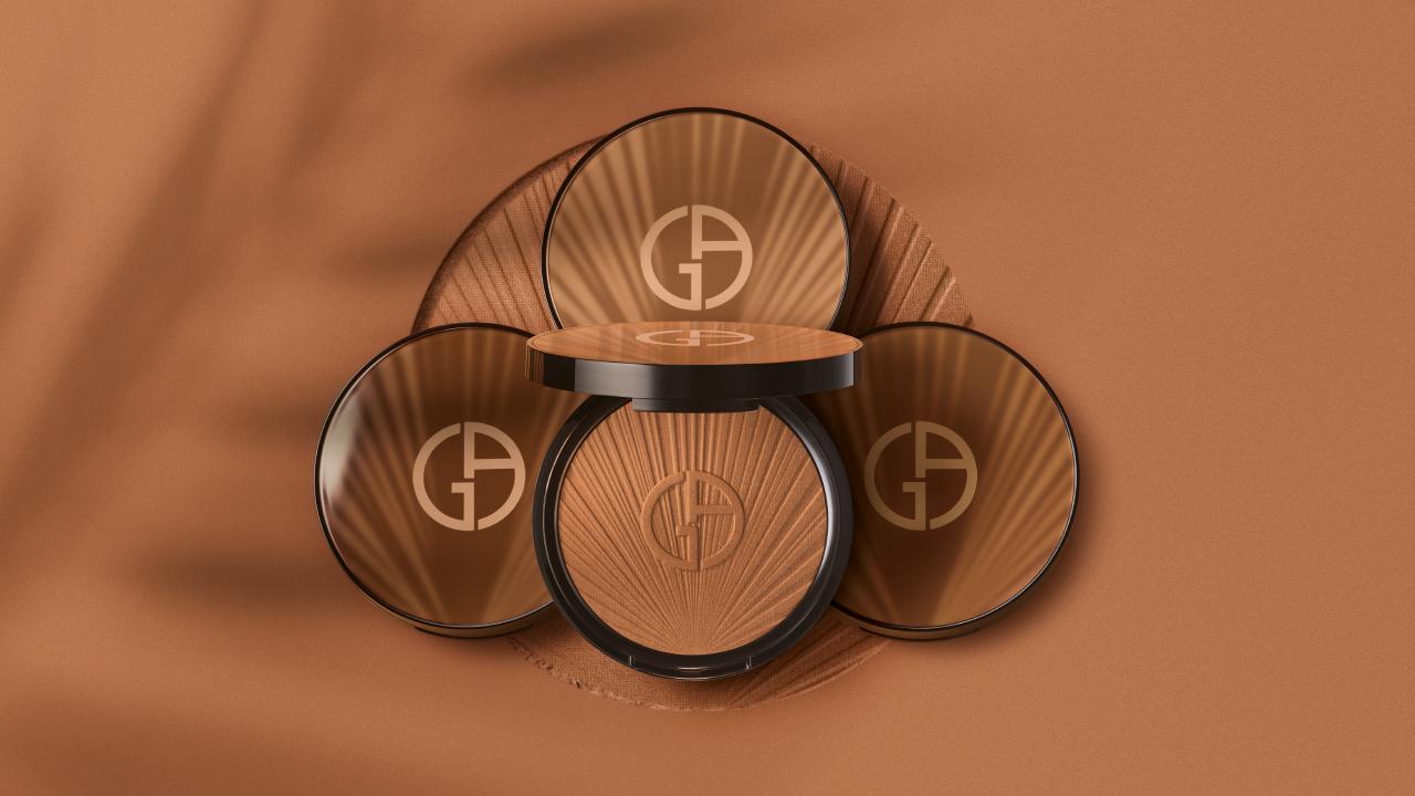 A sleek bronzer compact with the Giorgio Armani logo, surrounded by complementary bronzer pans on a warm, textured background.