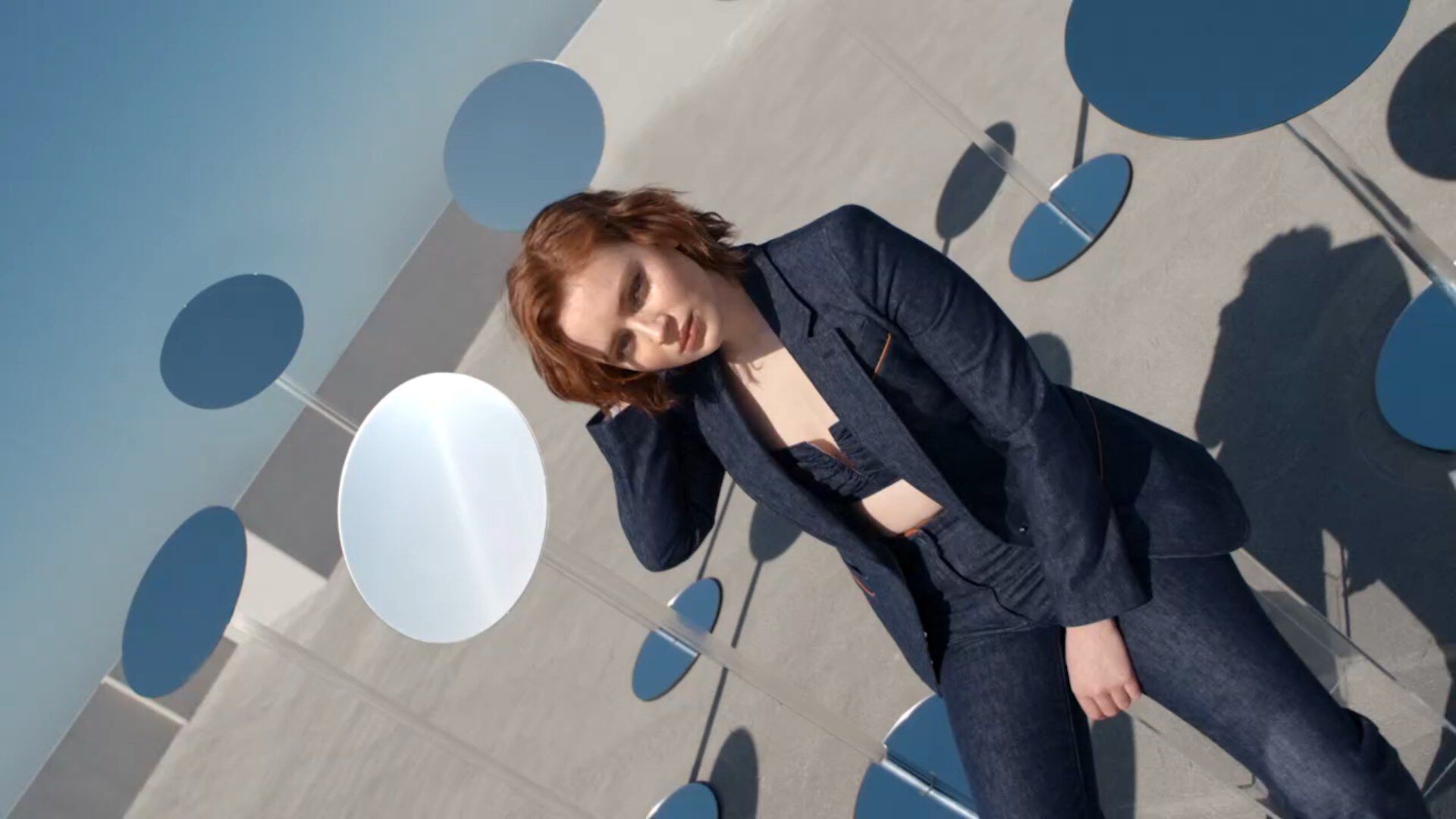 A young woman in a denim suit poses against abstract blue circles, showcasing a stylish rooftop fashion shoot.